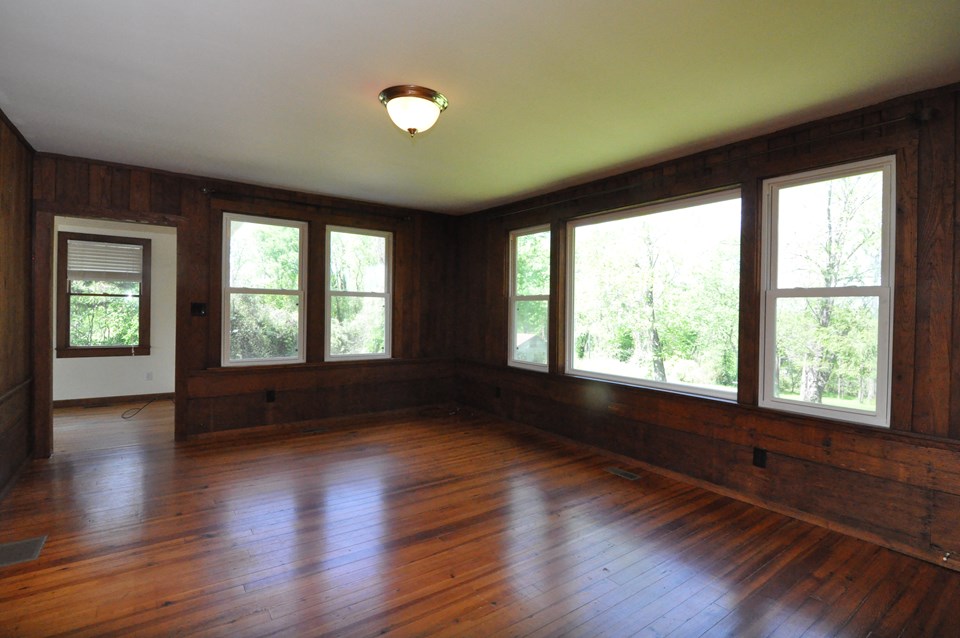 living room the living room is 18 x 13.8 and paneled in wormy chestnut from the old hotel as well as the heart pine floor which also is used on several of the other rooms. looking out the back windows you will see a view of the vacant lots dotted with trees and covered in grass. the door goes to the dining room.